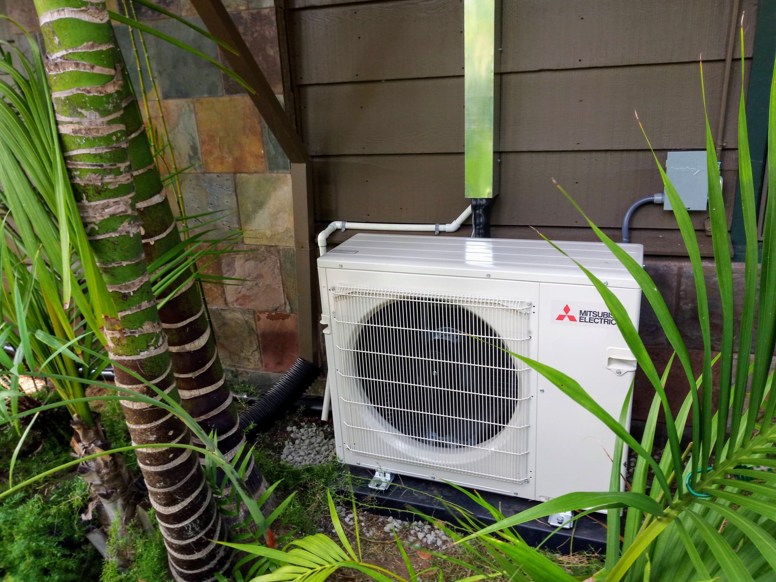 Mitsubishi Mini Split outdoor unit installed outside near the house, next to plants.