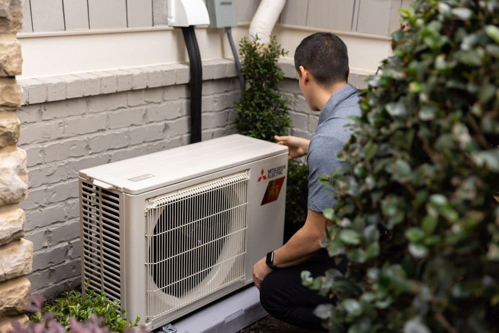 An HVAC installer is installing an outdoor Mitsubishi mini-split unit.