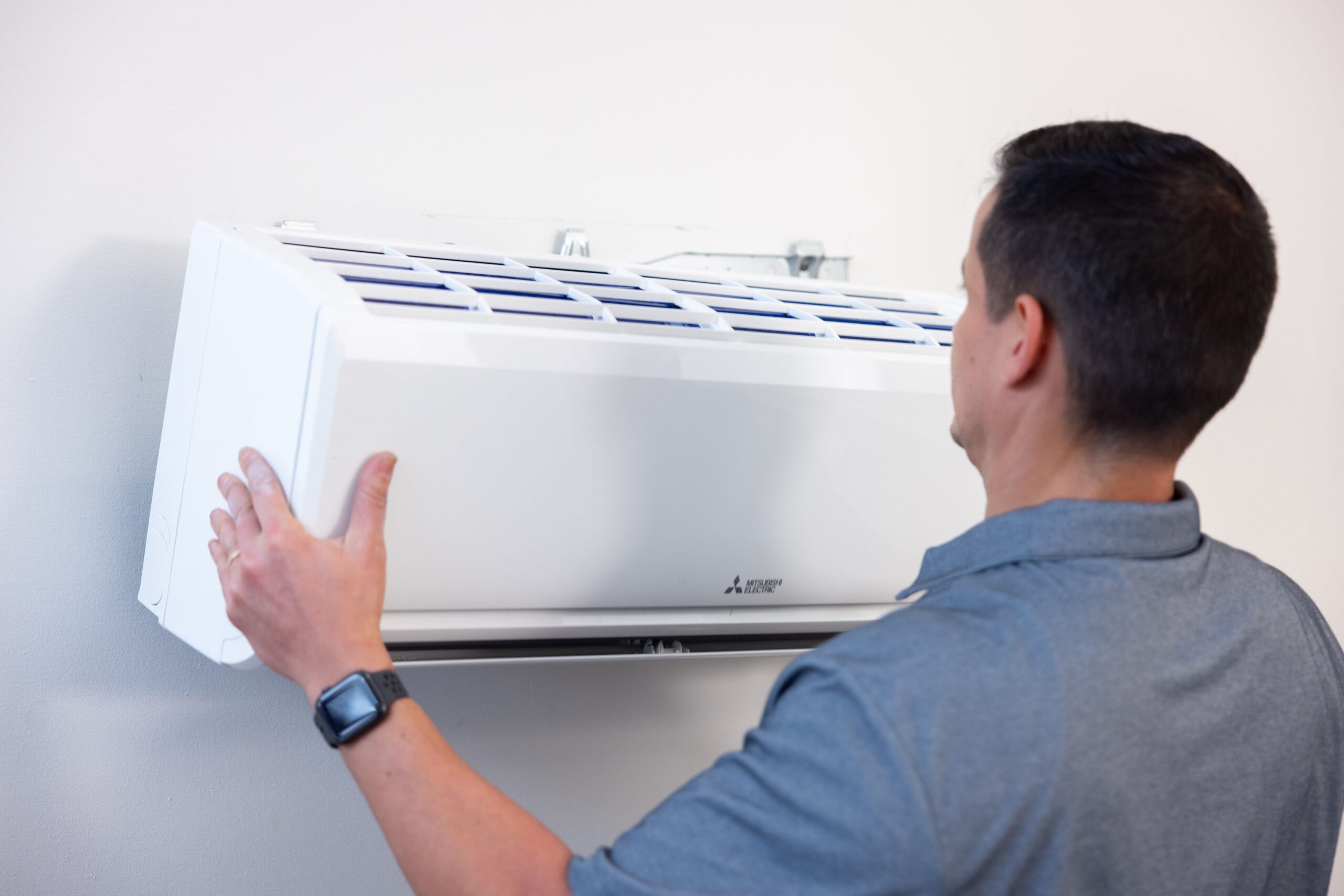 An HVAC installer installs a wall-mounted Mitsubishi mini-split unit.